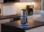 A 3D render of a sleek, screenless OpenAI smart speaker with subtle glowing neon accents resting on a modern kitchen counter, featuring clean floating glass UI panels.